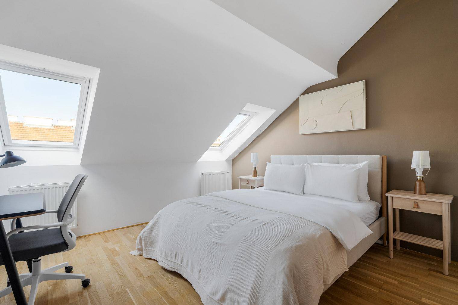 Gemütliches Schlafzimmer im Dachgeschoss mit Dachfenstern, Holzboden und Arbeitsbereich.