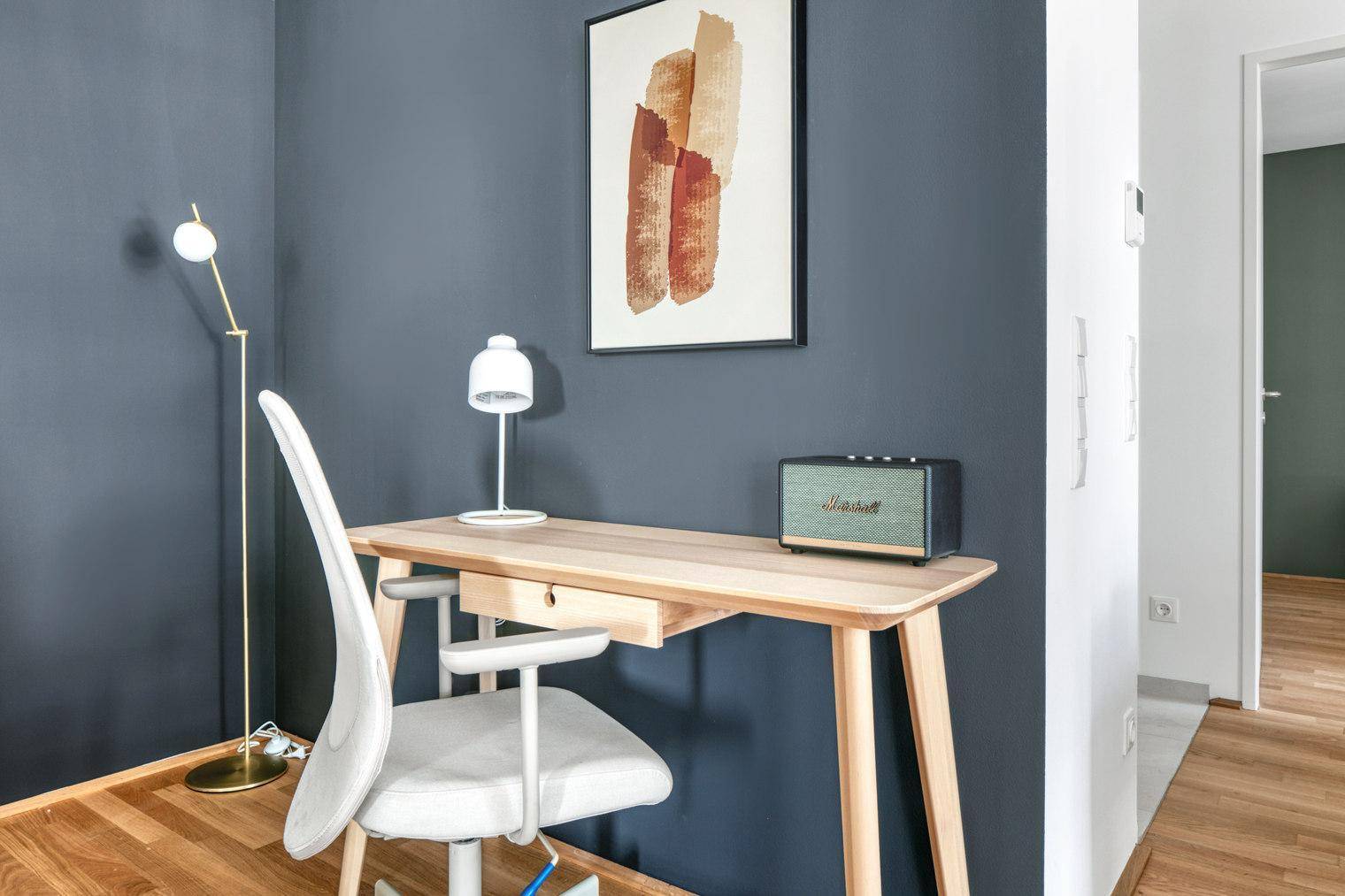 Heller Arbeitsbereich mit Schreibtisch, Stuhl und moderner Dekoration an der Wand.