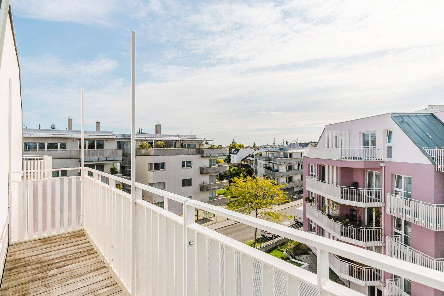 Balkon mit Holzboden und Blick auf die umliegenden Wohngebäude und die städtische Umgebung.