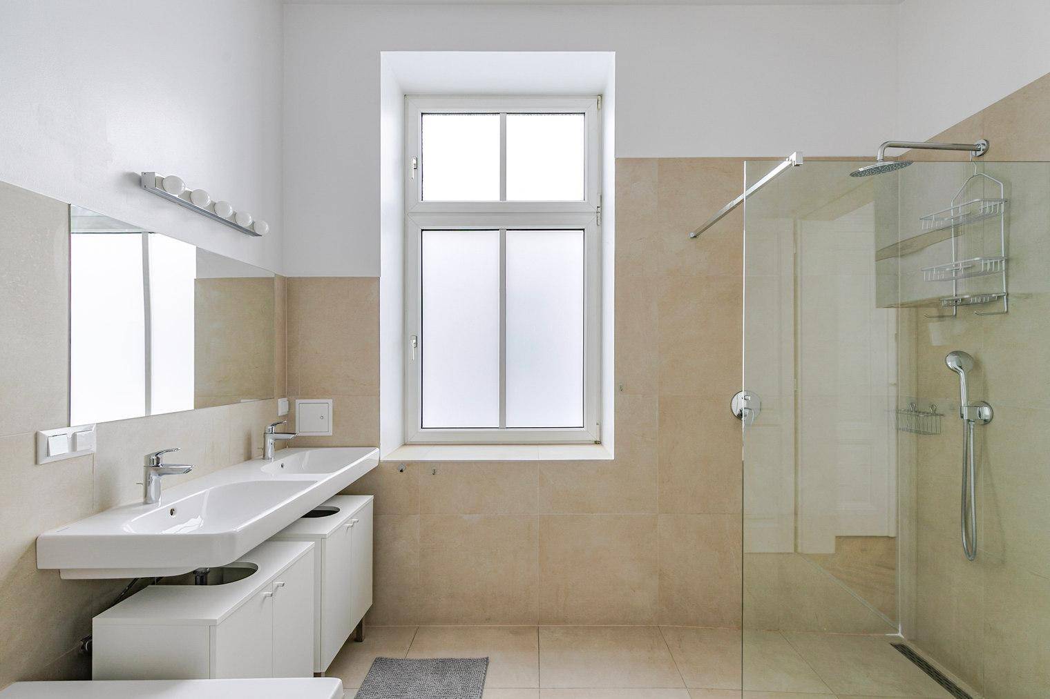 Modernes Badezimmer mit Doppelwaschbecken, großer Dusche und beigen Fliesen.