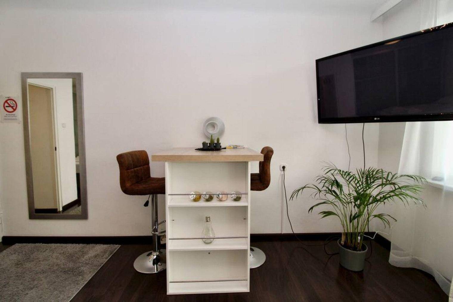 Moderner Bartisch mit zwei Hockern und Wandfernseher in einem hellen Wohnbereich.