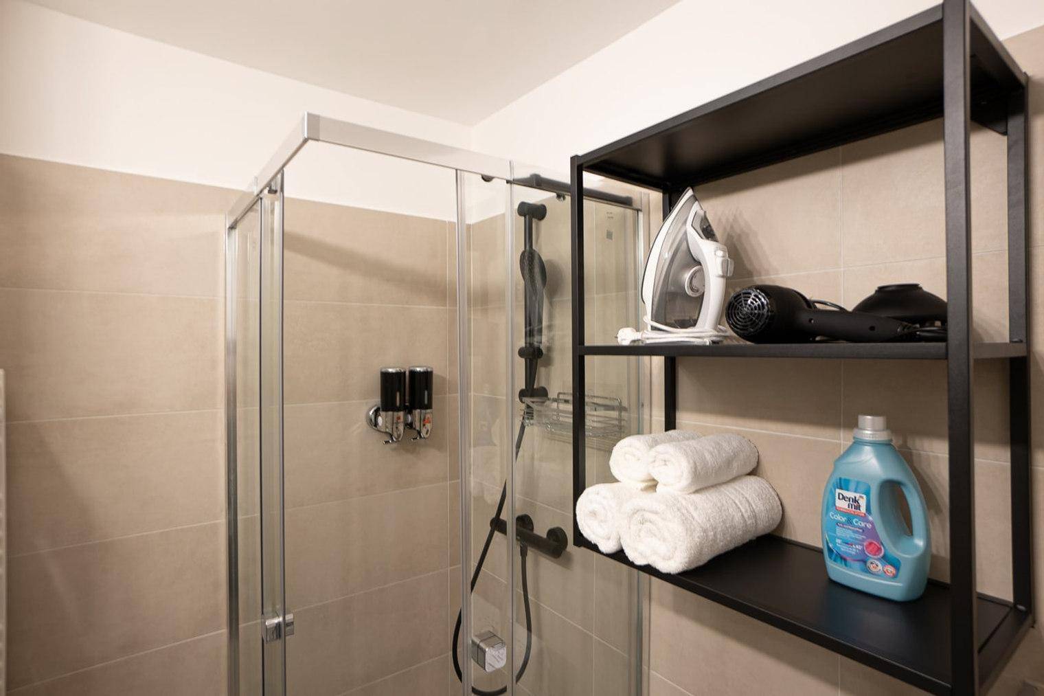 Duschbereich im Badezimmer mit Regal, Handtüchern und Pflegeprodukten, ordentlich präsentiert.