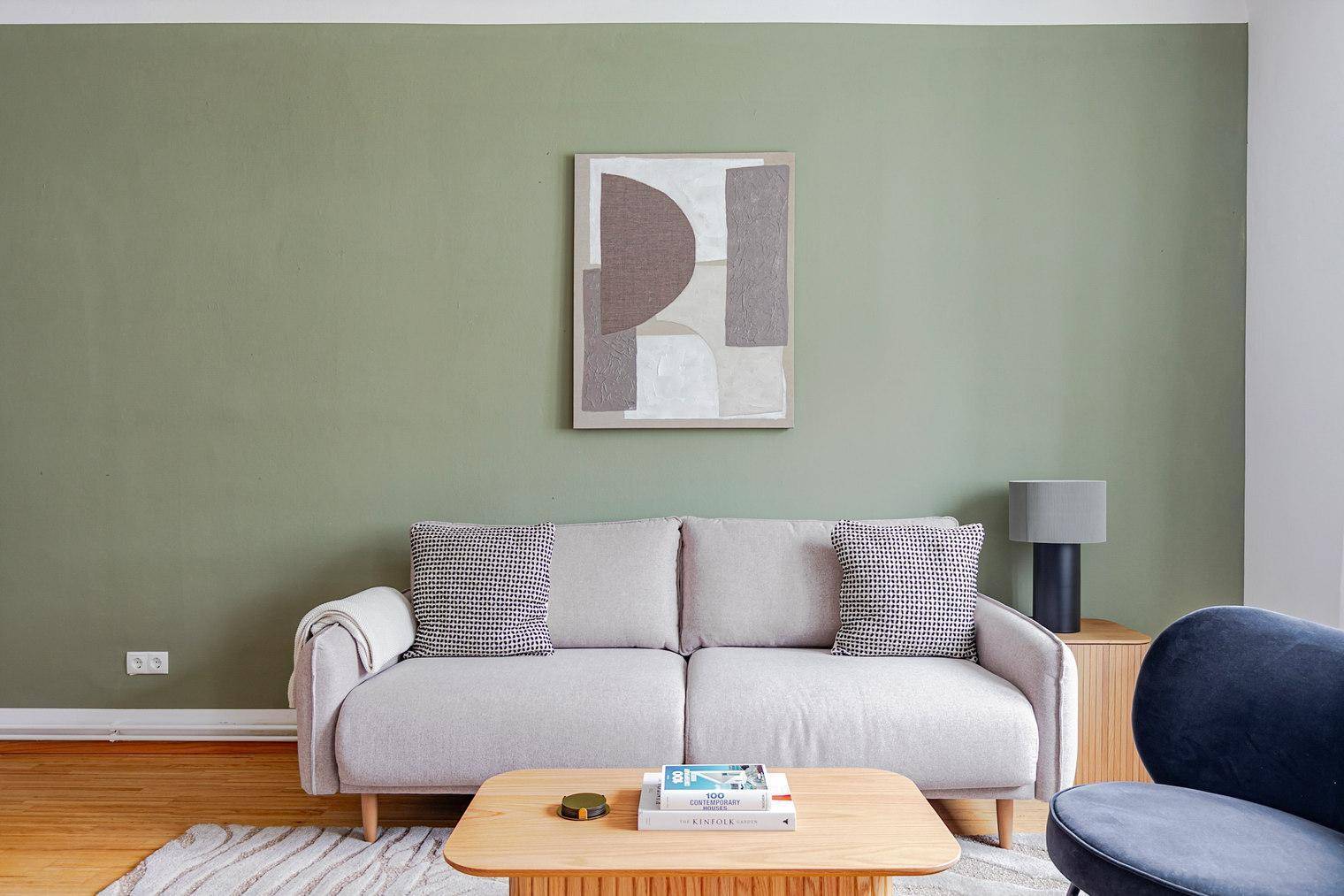 Detailansicht des Wohnzimmers mit beigem Sofa, abstraktem Bild und grüner Akzentwand.