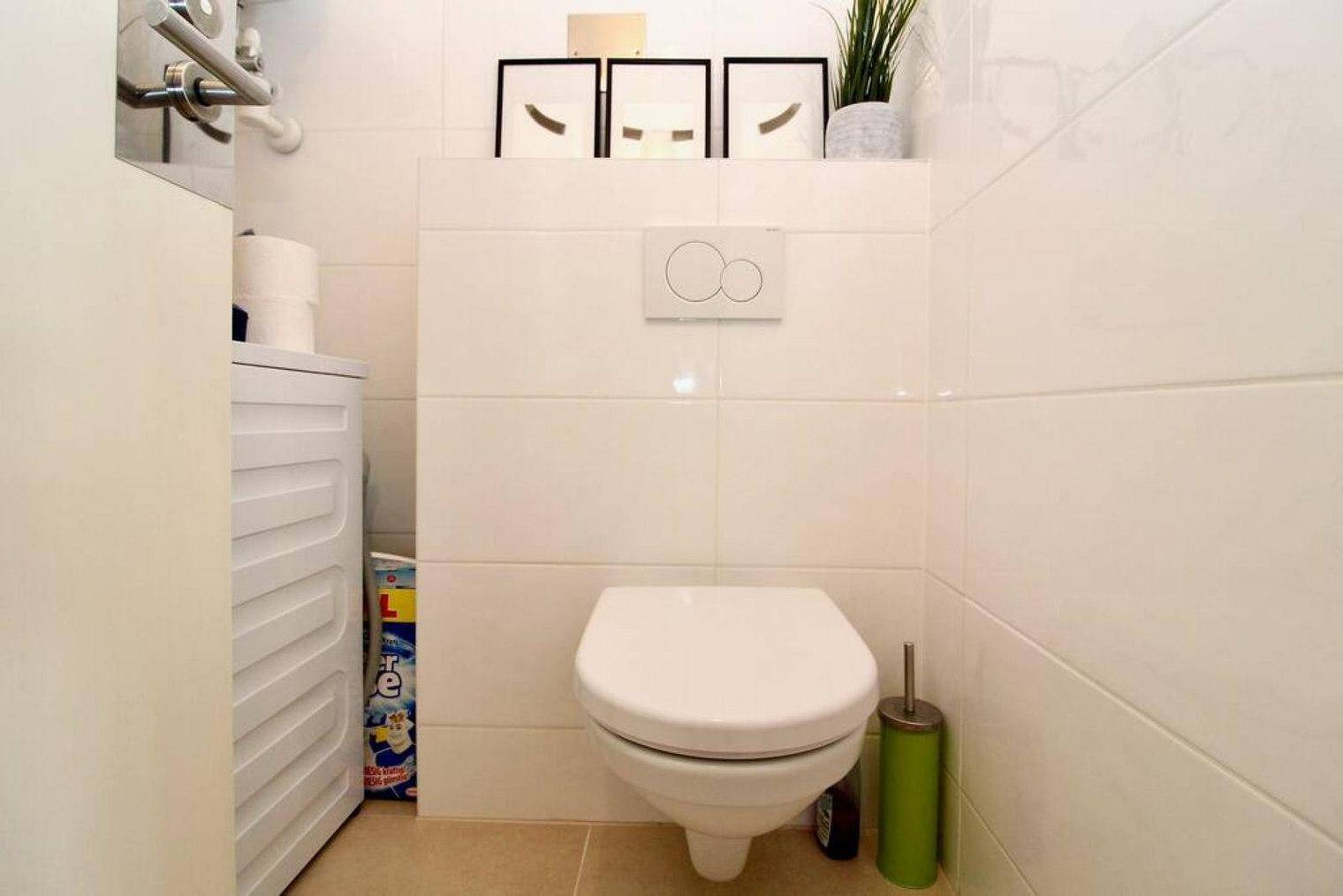 Separates WC mit wandhängender Toilette und weißen Fliesen.