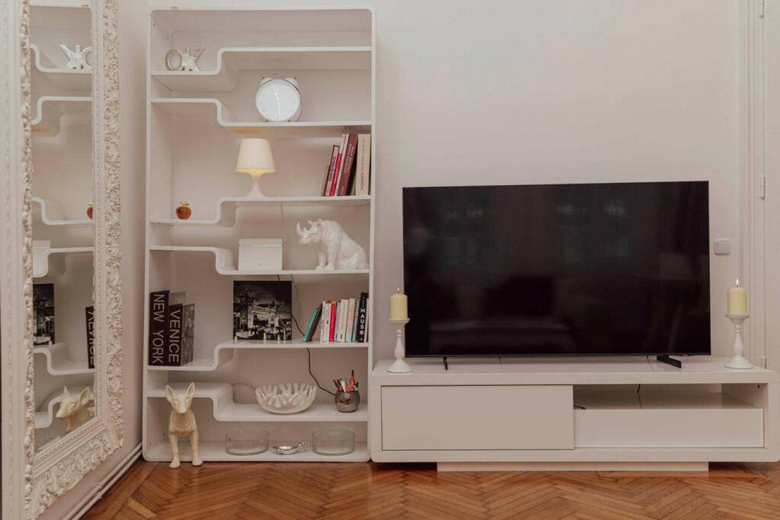 Moderner Fernseher auf einem Lowboard neben einem einzigartigen weißen Bücherregal mit Dekoration.