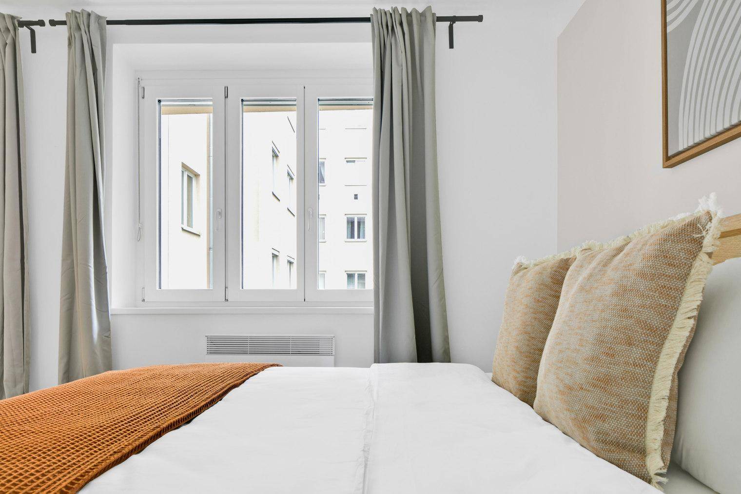 Schlafzimmer mit großem Fenster, das viel Tageslicht hereinlässt und Vorhängen.