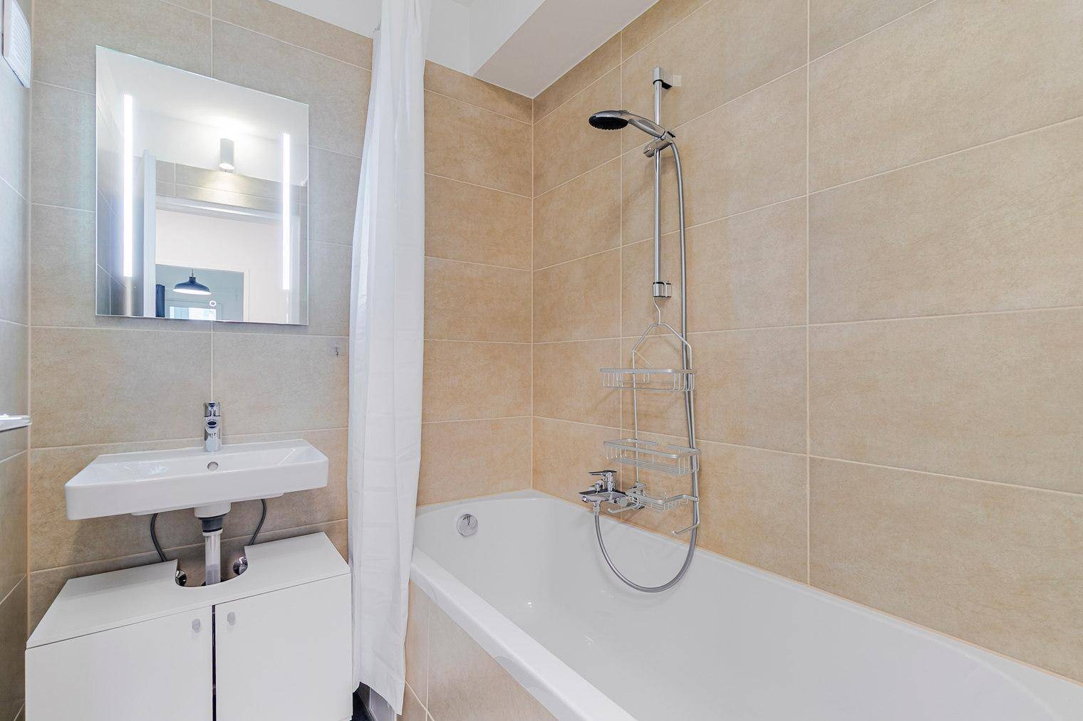 Modernes Badezimmer mit Badewanne, Duschvorhang und einem Waschbecken mit Spiegelschrank.