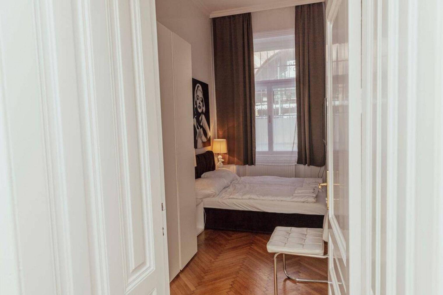 Blick in ein Schlafzimmer mit Doppelbett, Kleiderschrank und Fenster mit dunklen Vorhängen.
