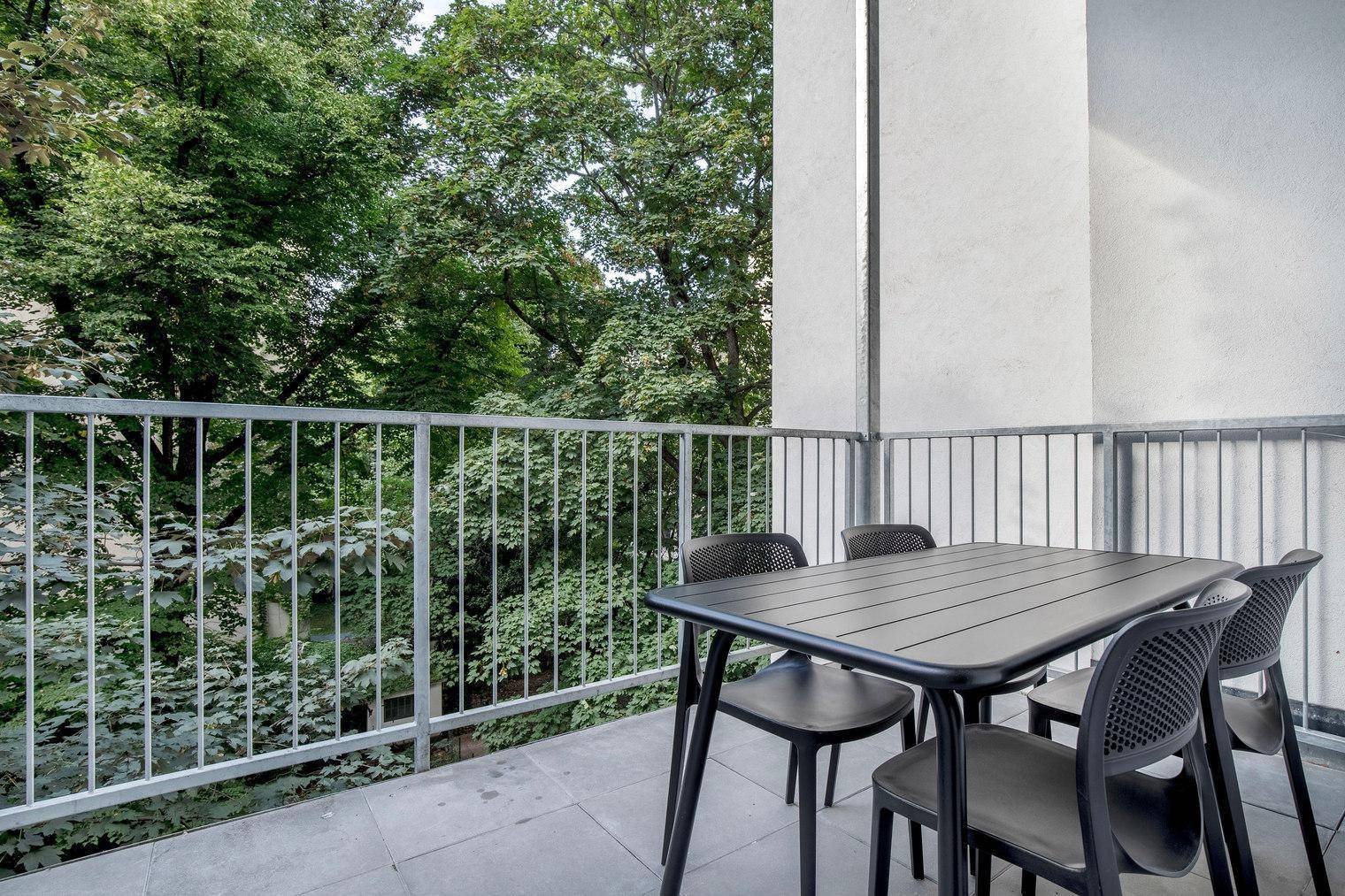 Balkon mit Esstisch und Stühlen, umgeben von üppigem Grün und Bäumen.