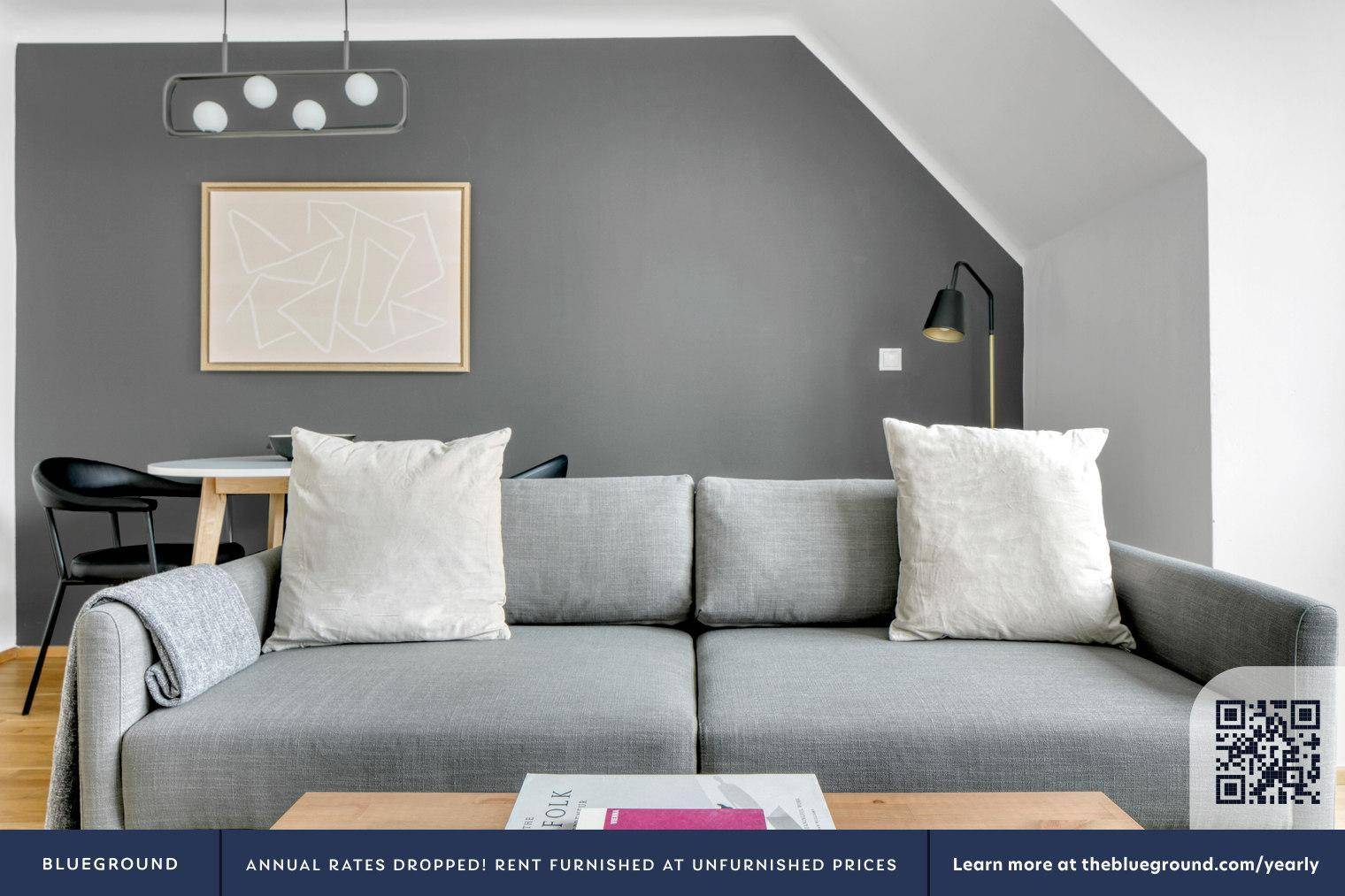 Modern eingerichtetes Wohnzimmer mit grauem Sofa, Kunst an der Wand und schräger Decke.