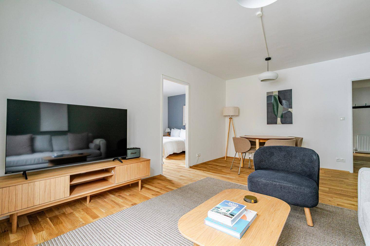 Offener Wohnbereich mit Fernseher, Esstisch und Blick auf ein angrenzendes Schlafzimmer.