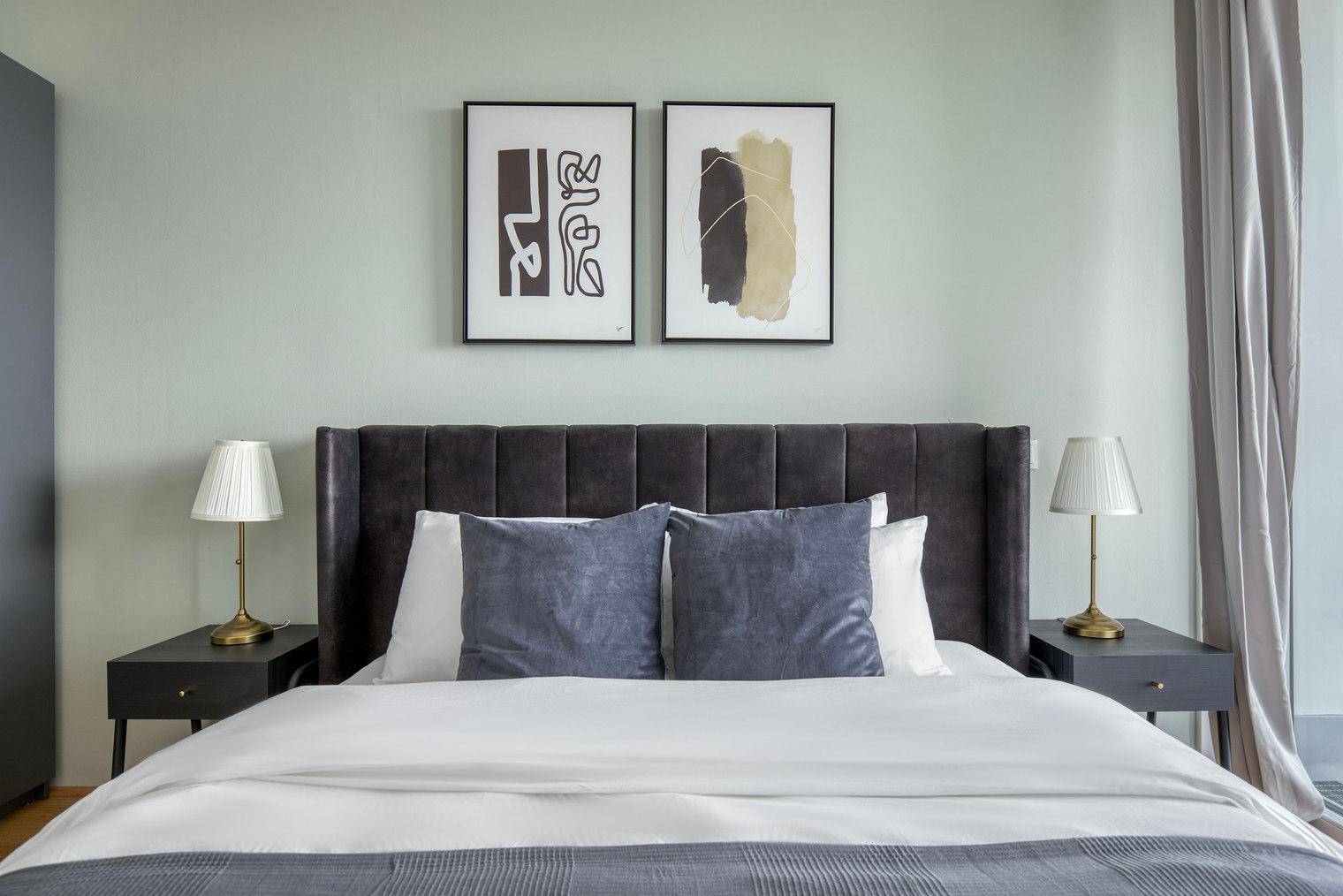 Gemütliches Doppelbett mit gepolstertem Kopfteil und moderner Kunst an der Wand.