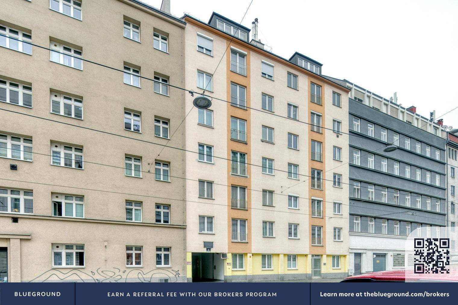 Ansicht einer belebten Straße mit mehreren Mehrfamilienhäusern und Straßenbahnschienen.
