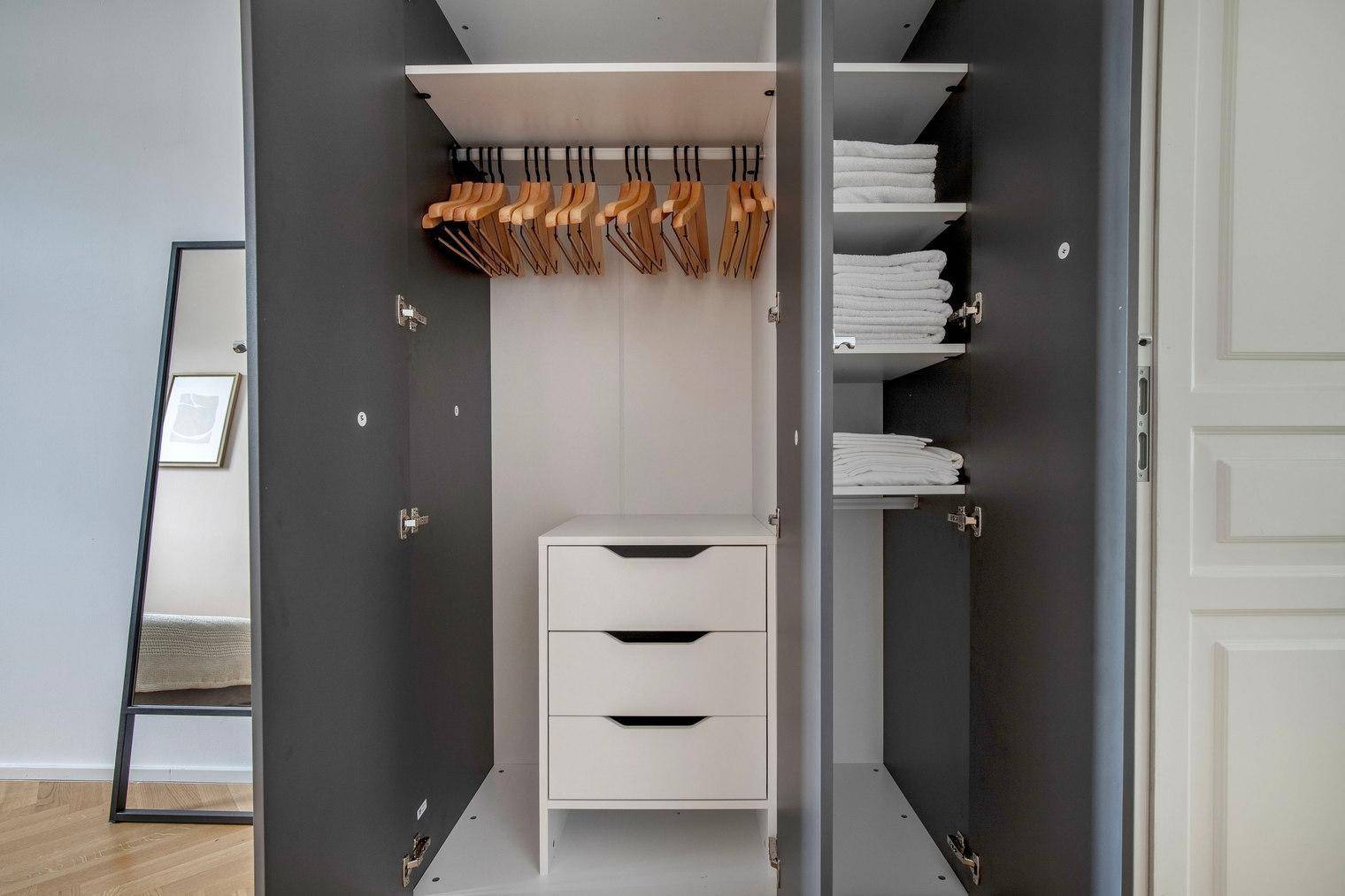 Offener Kleiderschrank mit Kleiderstangen, Schubladen und Regalen für Wäsche.