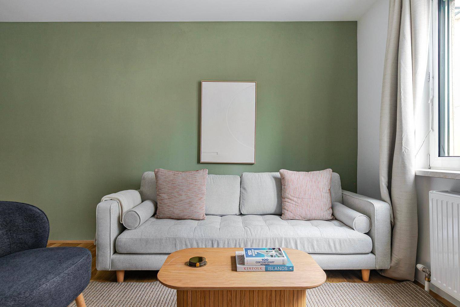 Gemütliches Sofa mit Kissen in einem hellen Wohnzimmer mit grüner Akzentwand.