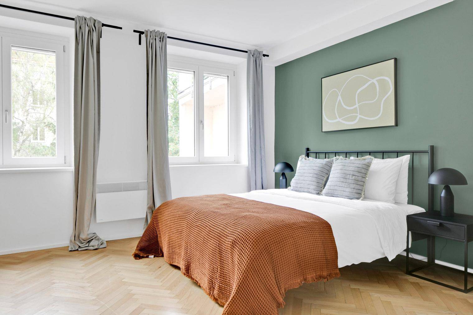 Schlafzimmer mit Holzboden, Doppelbett und einer grünen Akzentwand.