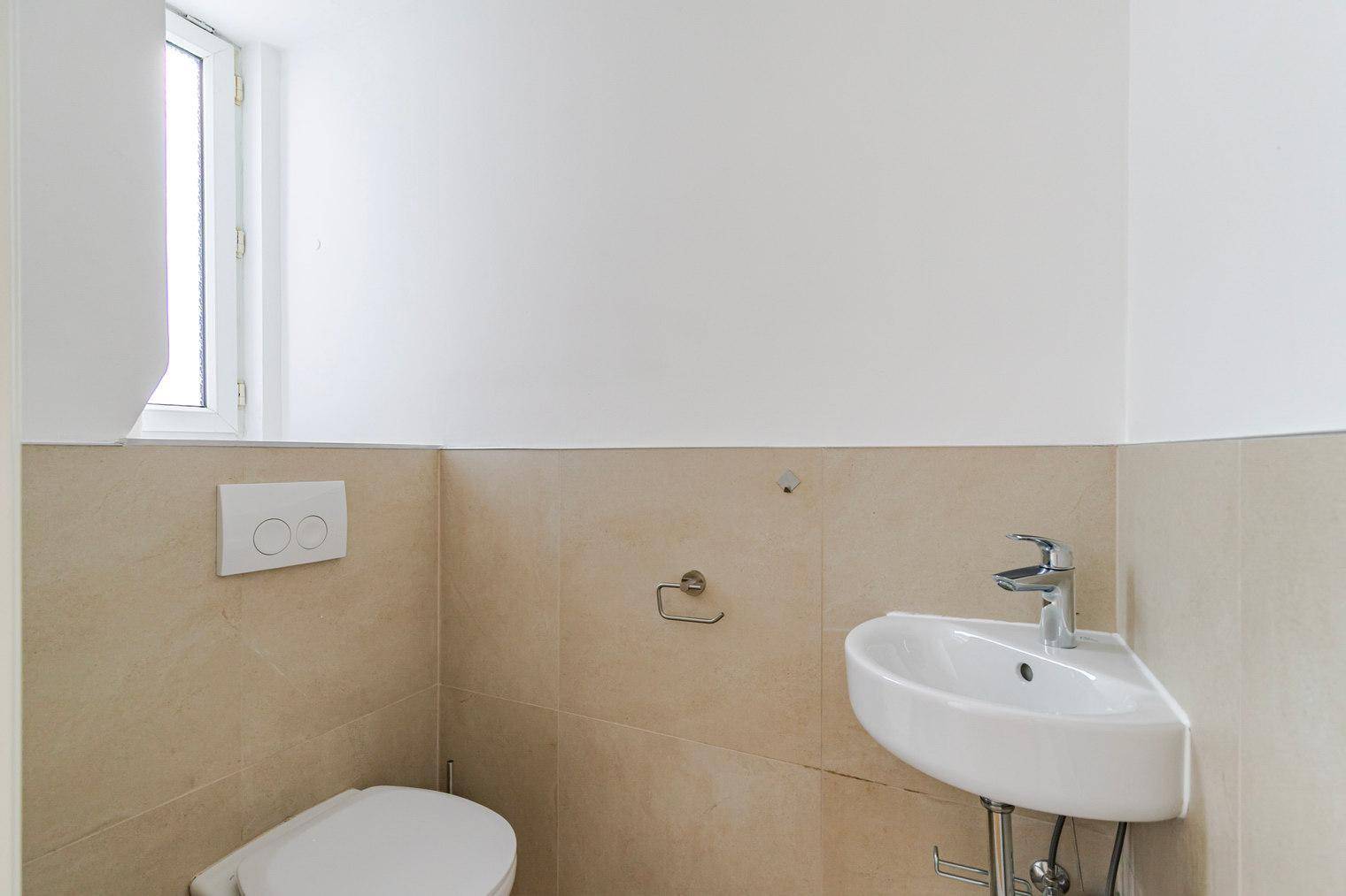 Separates Gäste-WC mit kleinem Waschbecken und Fenster für natürliche Belüftung.