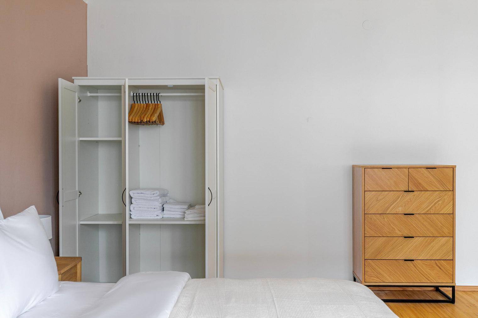 Schlafzimmer mit weißem Kleiderschrank, Kommode und Blick auf das Bett.