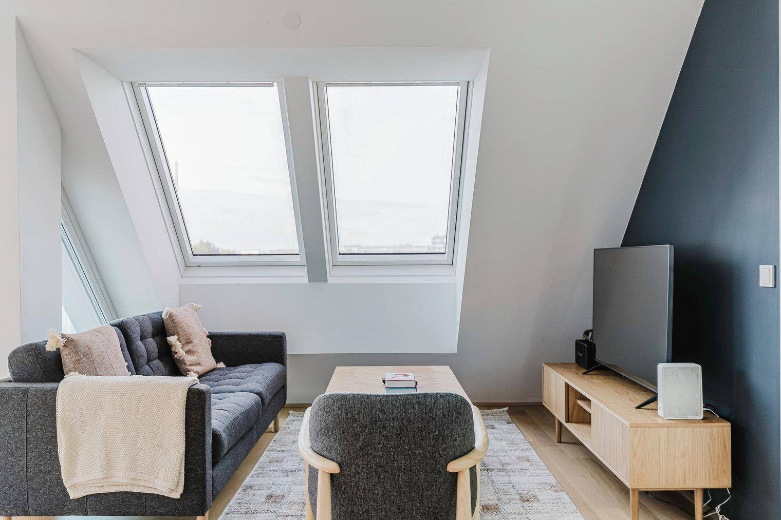 Gemütliches Wohnzimmer mit Dachschrägen, modernen Möbeln und einem dunklen Akzentwandbereich.