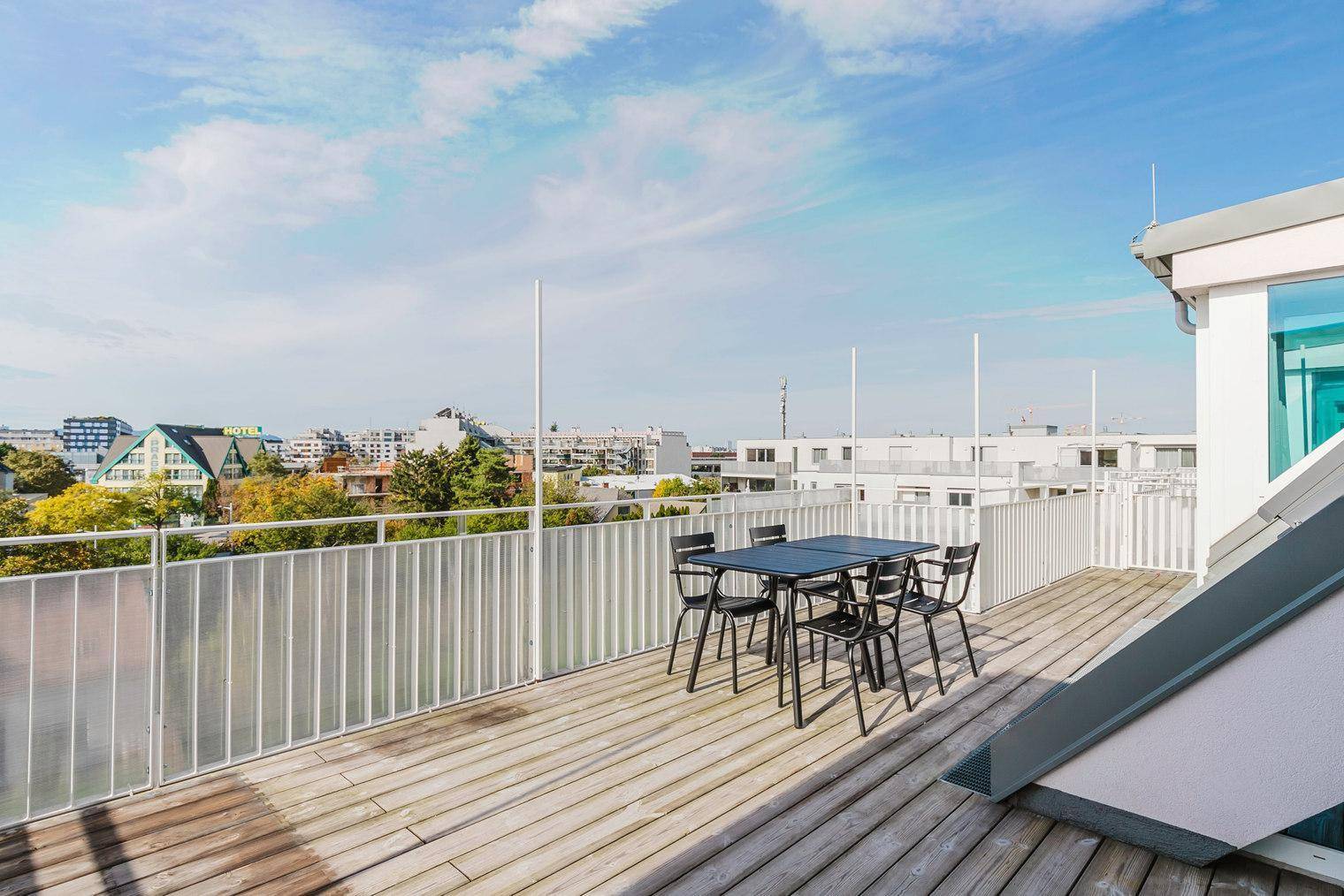Geräumige Dachterrasse mit Holzboden und Esstisch, bietet einen weiten Blick über die Stadt.