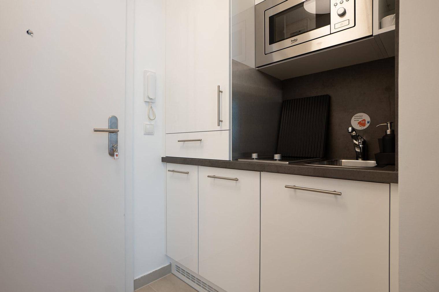 Moderne Küchenzeile mit Mikrowelle, Kochfeld und Spüle neben der Eingangstür, platzsparend.