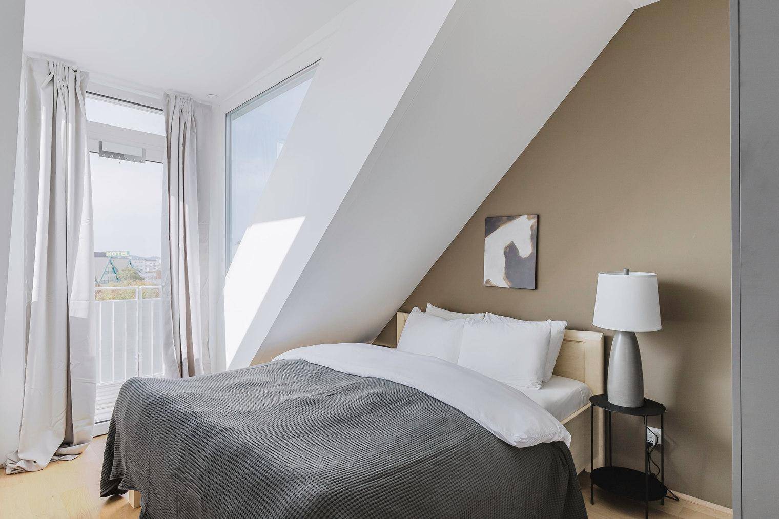 Helles Schlafzimmer mit Dachschräge, beigefarbener Akzentwand und Zugang zur Terrasse.