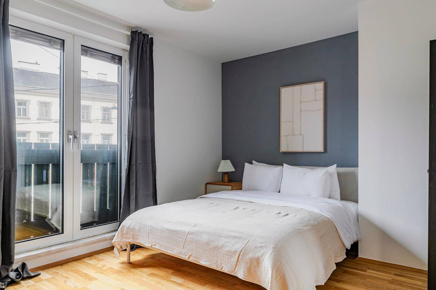 Schlafzimmer mit Doppelbett, blauer Akzentwand und Zugang zu einem französischen Balkon.