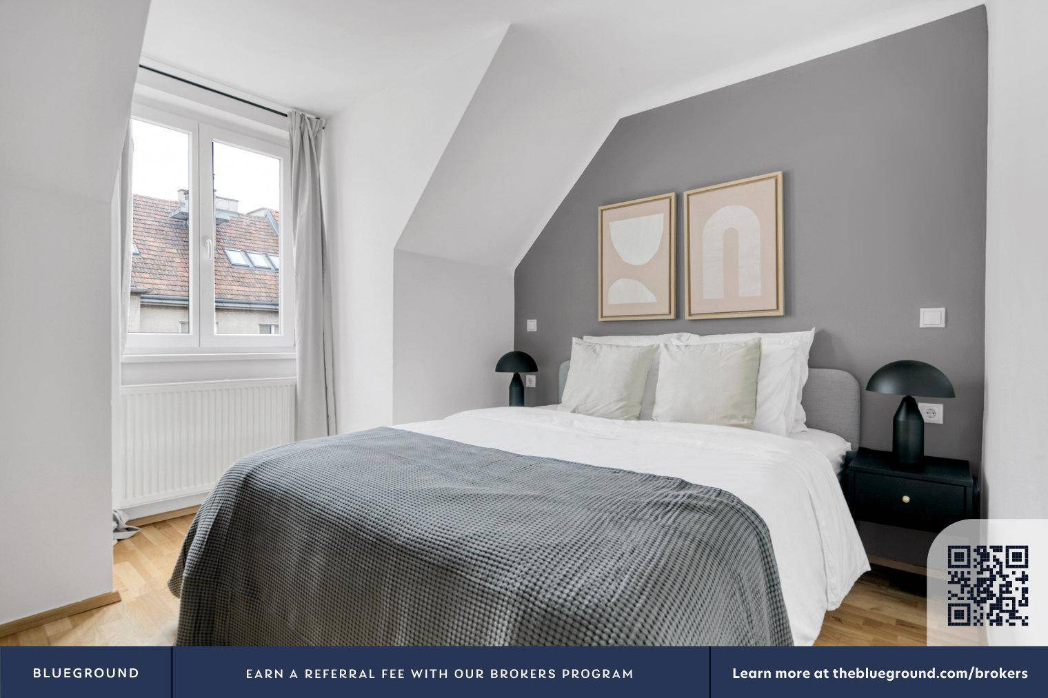 Gemütliches Schlafzimmer mit Doppelbett, schräger Decke und Fenster mit Blick auf die Dächer.