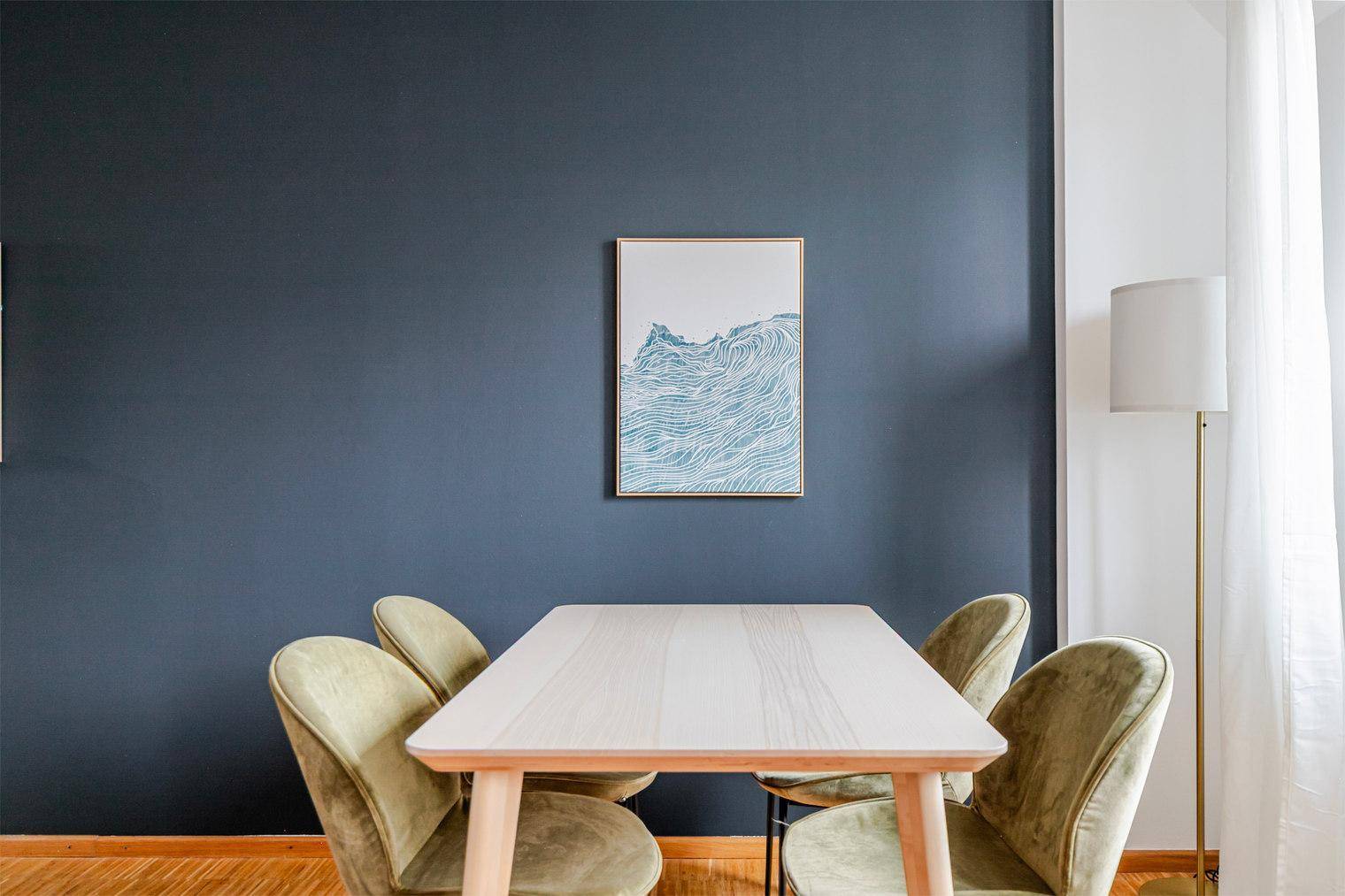 Essbereich mit modernem Holztisch und grünen Samtstühlen vor einer dunkelblauen Wand.