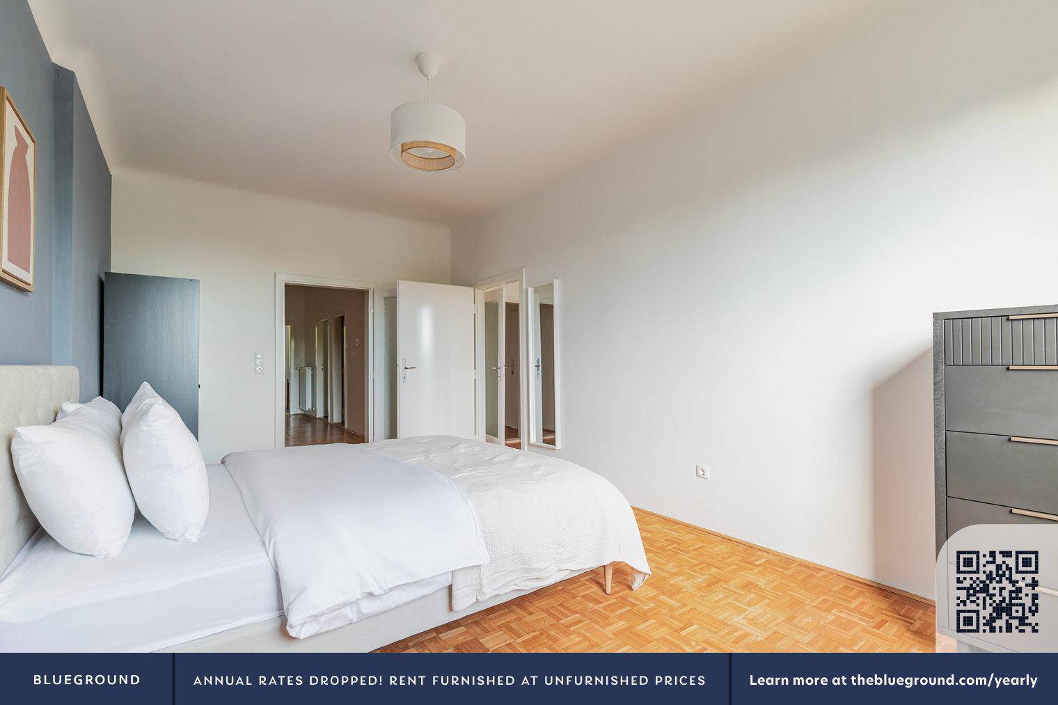 Schlafzimmer mit Holzboden, weißem Bett und Blick auf den Flur durch eine offene Tür.