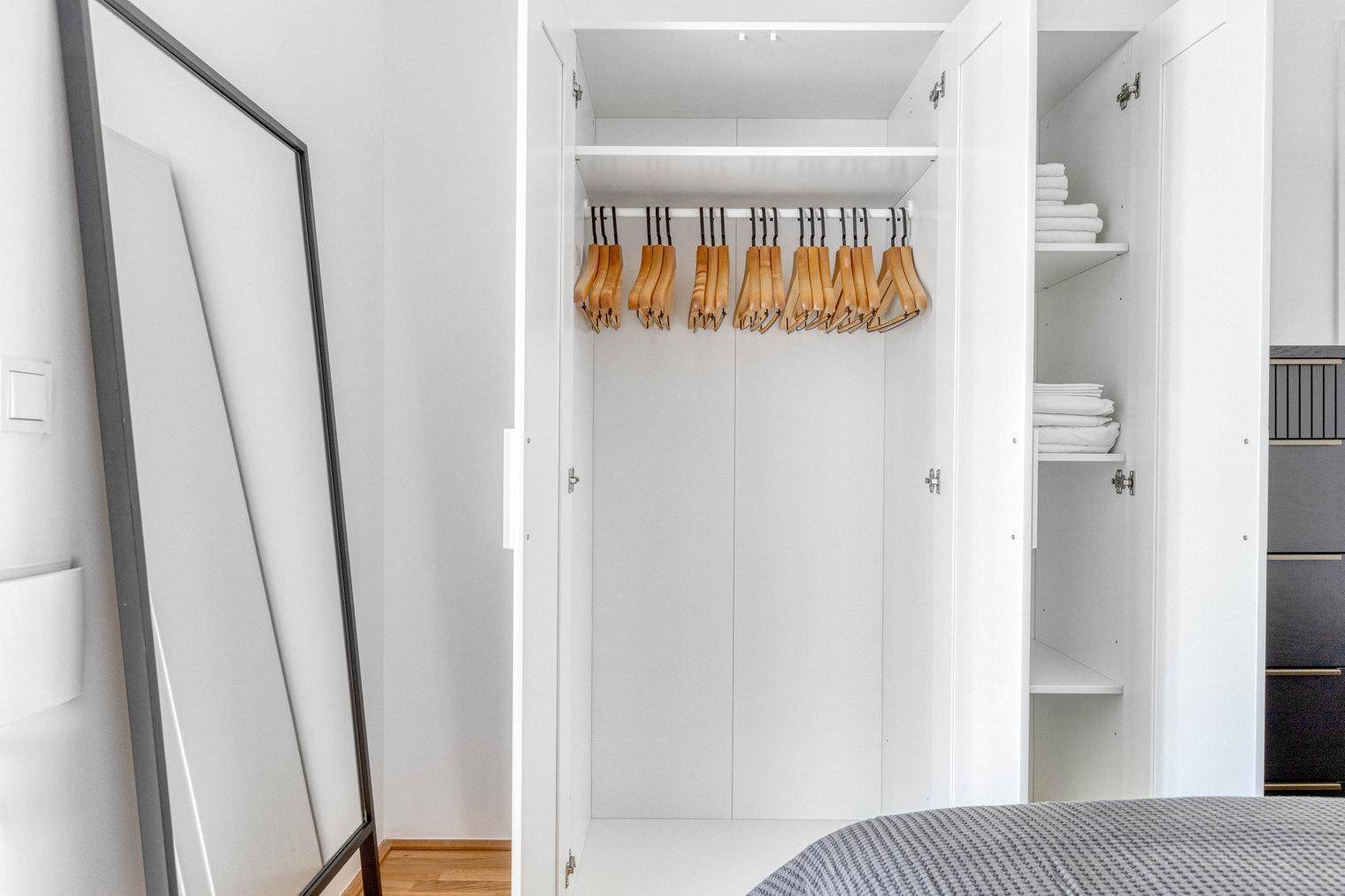 Schlafzimmer mit offenem Kleiderschrank und Ganzkörperspiegel.