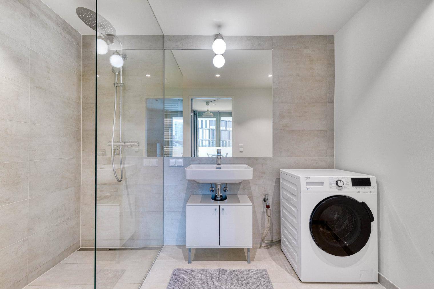 Modernes Badezimmer mit begehbarer Dusche, Waschbecken und Waschmaschine.