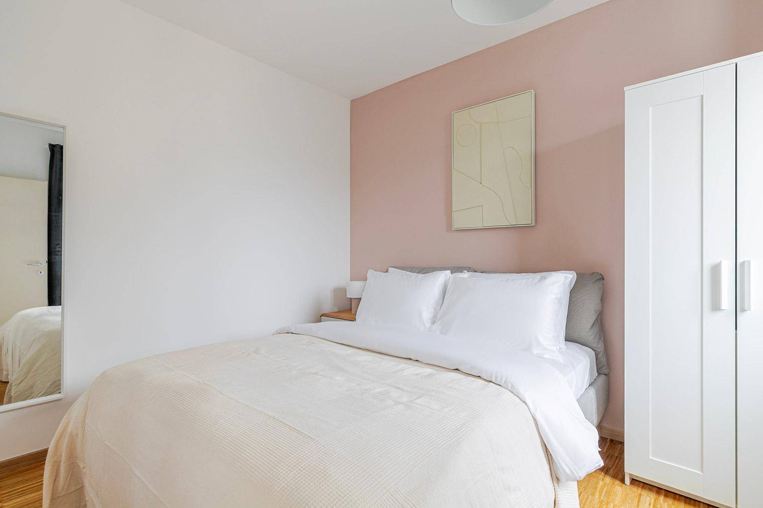 Helles Schlafzimmer mit Doppelbett, weißem Kleiderschrank und Spiegel.