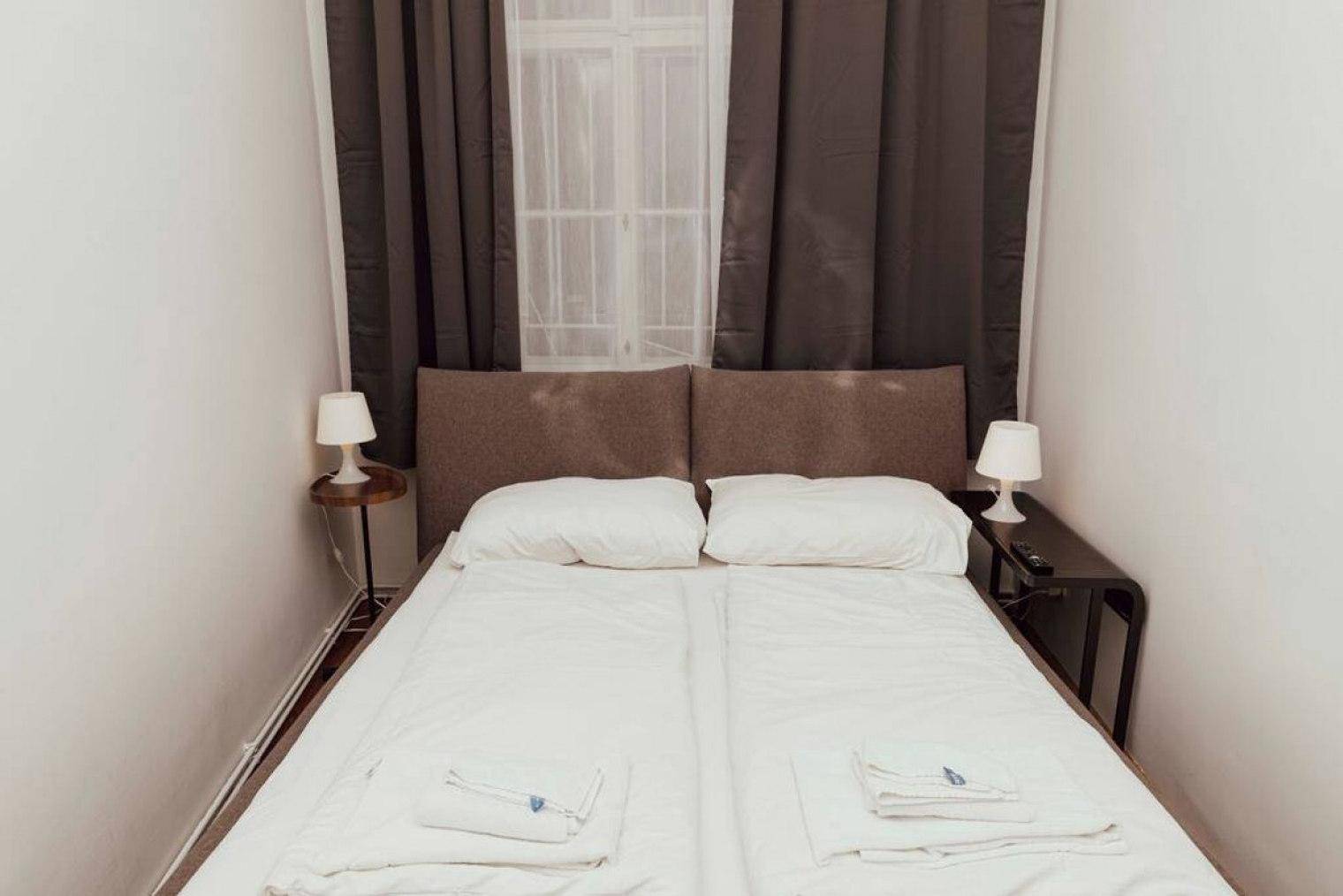 Gemütliches Schlafzimmer mit Doppelbett, weißen Nachttischen und dunklen Vorhängen.