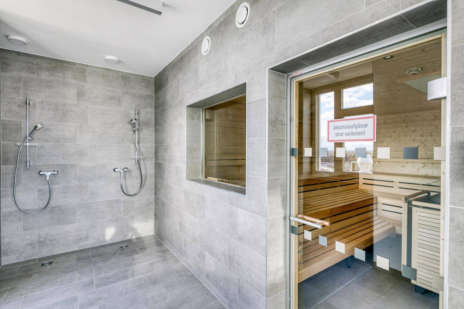 Moderner Wellnessbereich mit großer Dusche und holzverkleideter Sauna.