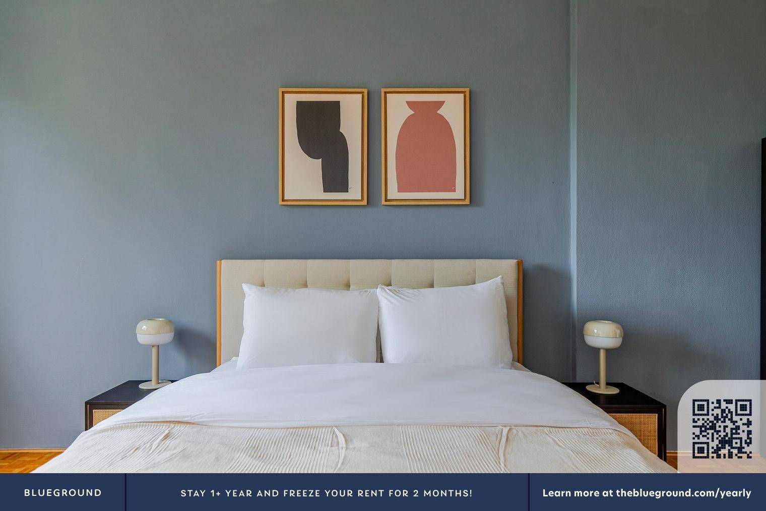 Nahaufnahme des Doppelbettes mit weißen Kissen und Nachttischen vor einer blaugrauen Wand.