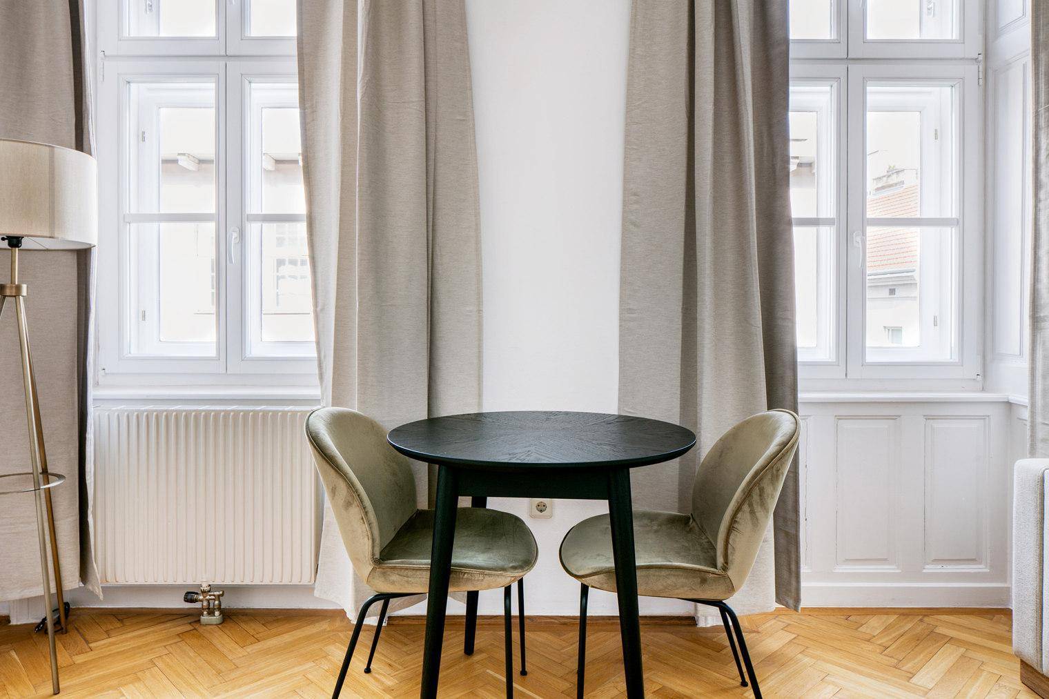 Gemütlicher Essbereich mit kleinem Tisch und zwei Stühlen vor großen Fenstern.