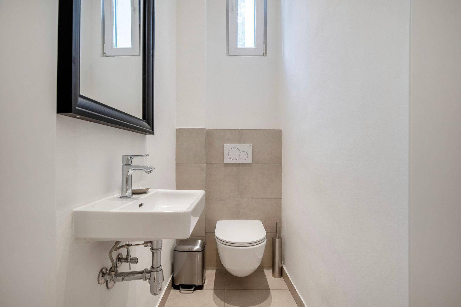 Kleines Gäste-WC mit wandhängendem WC, Waschbecken und Spiegel.