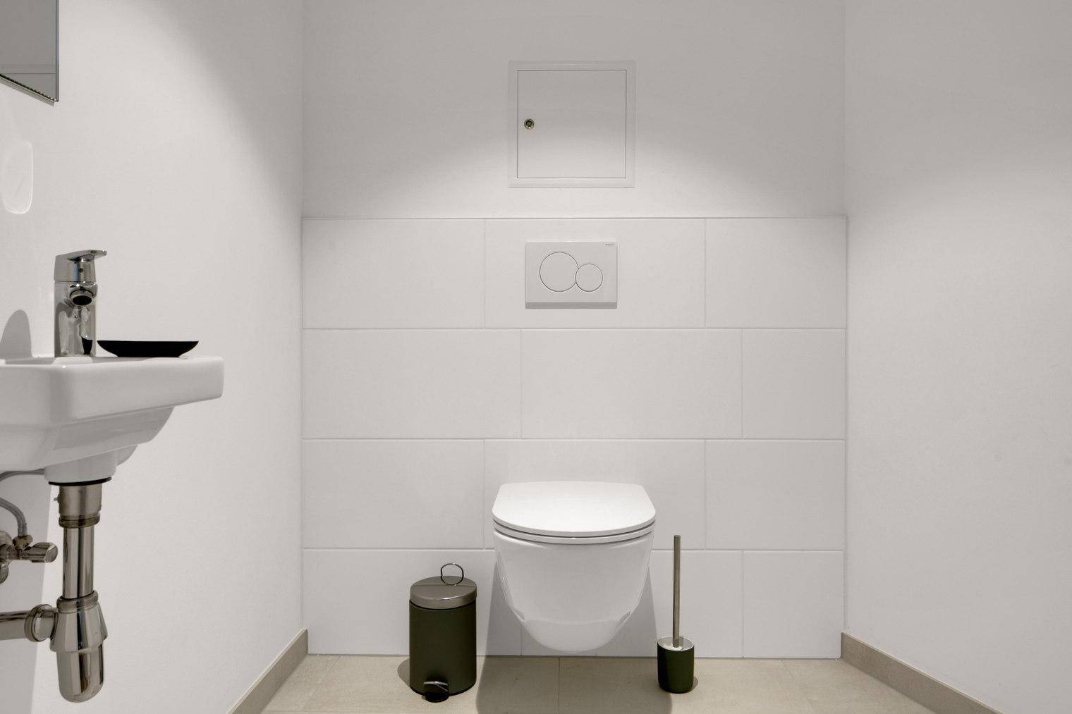 Separates WC mit wandhängender Toilette und kleinem Waschbecken in minimalistischem Design.