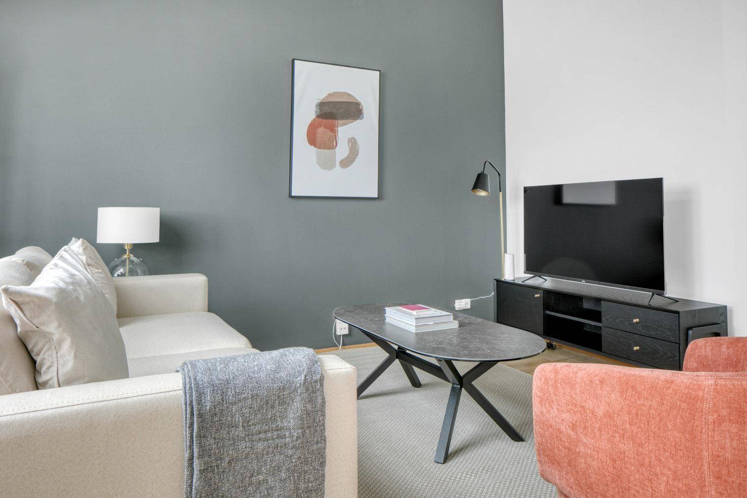 Gemütliches Wohnzimmer mit Sofa, Fernseher und moderner Kunst an der grauen Wand.