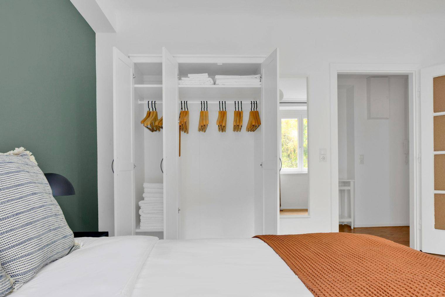 Offener weißer Kleiderschrank mit Kleiderbügeln und gefalteten Handtüchern.