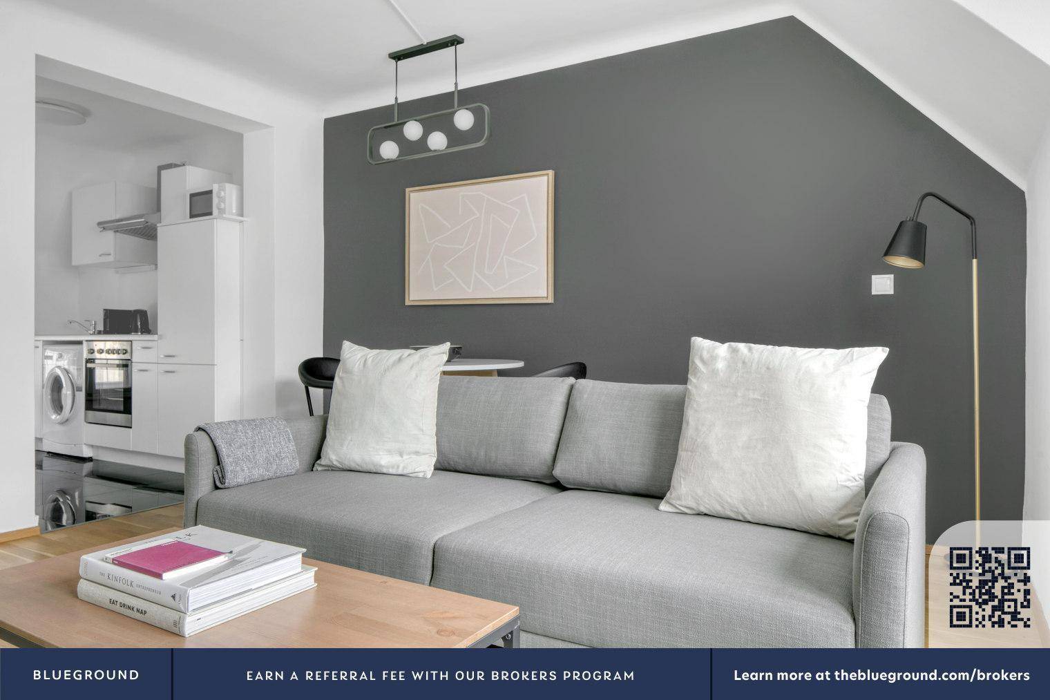 Wohnbereich mit grauem Sofa und angrenzender, kompakter Küchenzeile mit Waschmaschine.