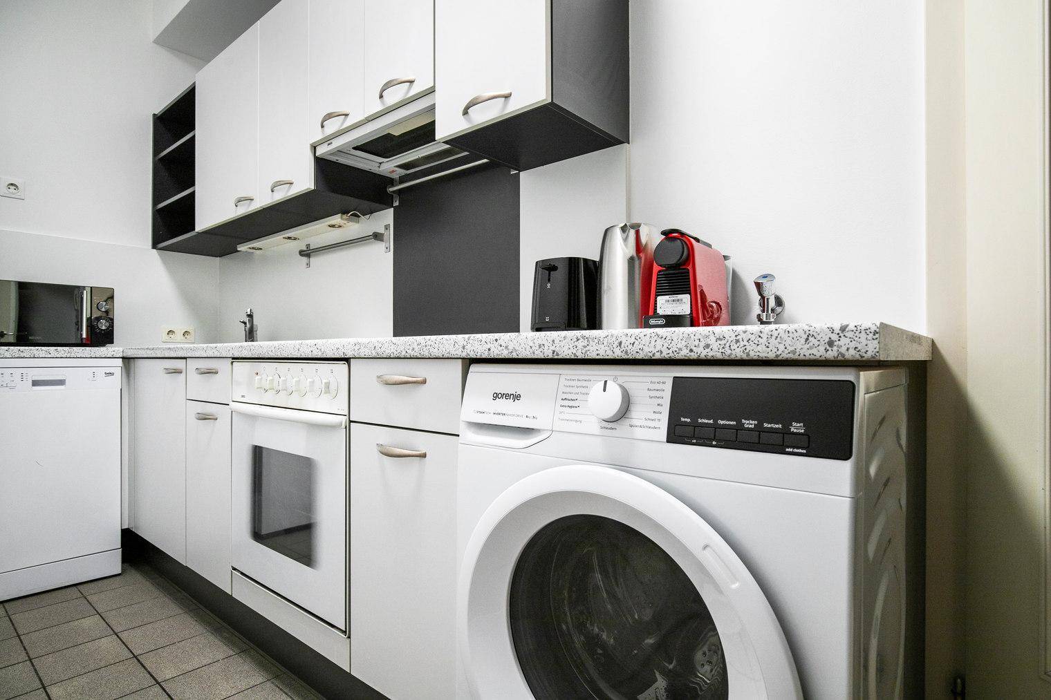 Küchenbereich mit integriertem Backofen, Waschmaschine und Arbeitsplatte.