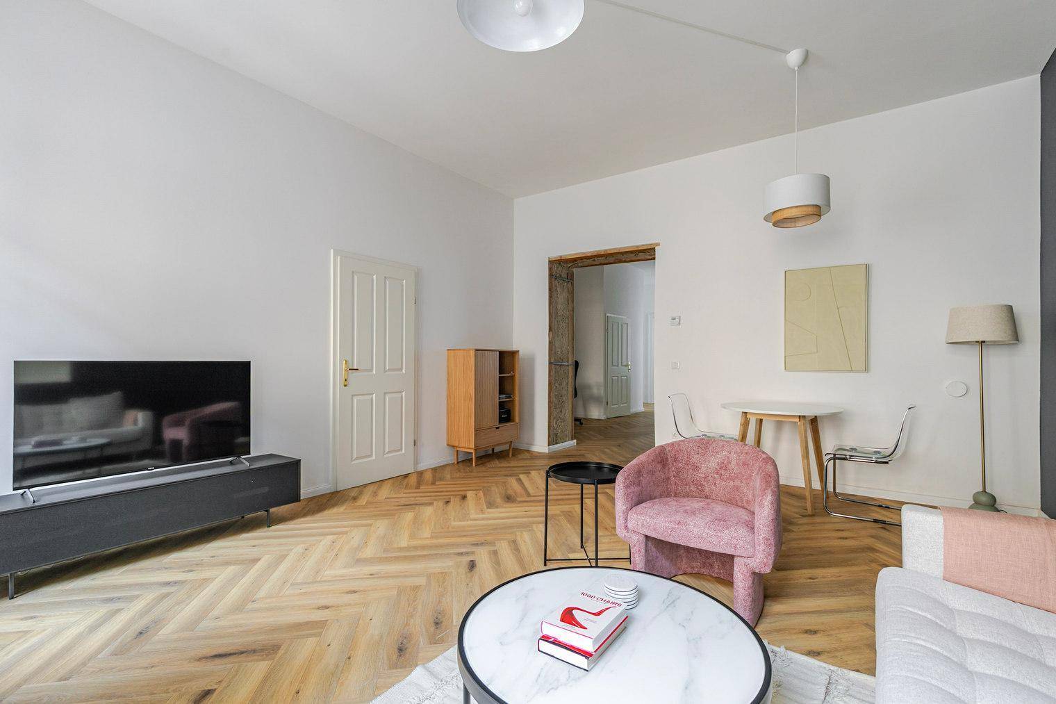 Geräumiges Wohnzimmer mit Fischgrätparkett, Essbereich und Zugang zu weiteren Räumen.