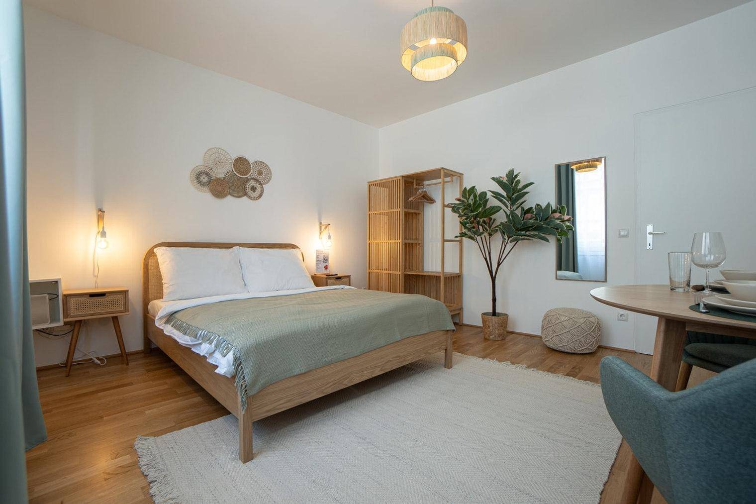 Gemütliches Schlafzimmer mit Holzbett, Esstisch und offener Garderobe in heller Atmosphäre.