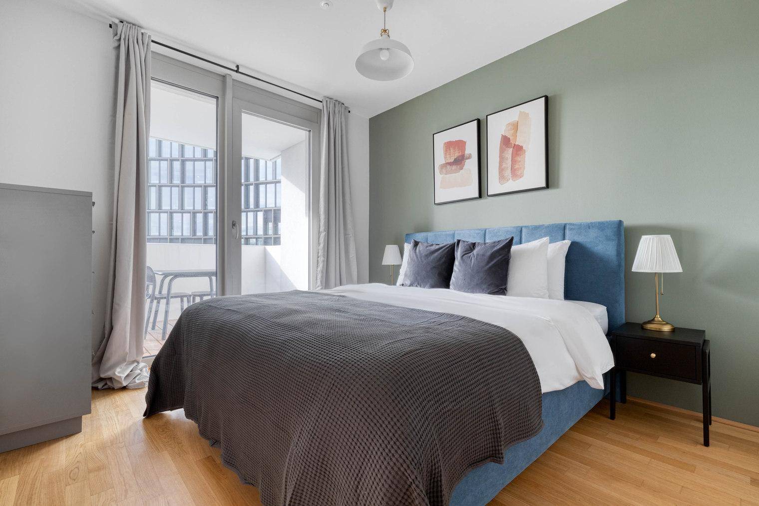 Helles Schlafzimmer mit Doppelbett, Holzboden und Zugang zu einem Balkon.