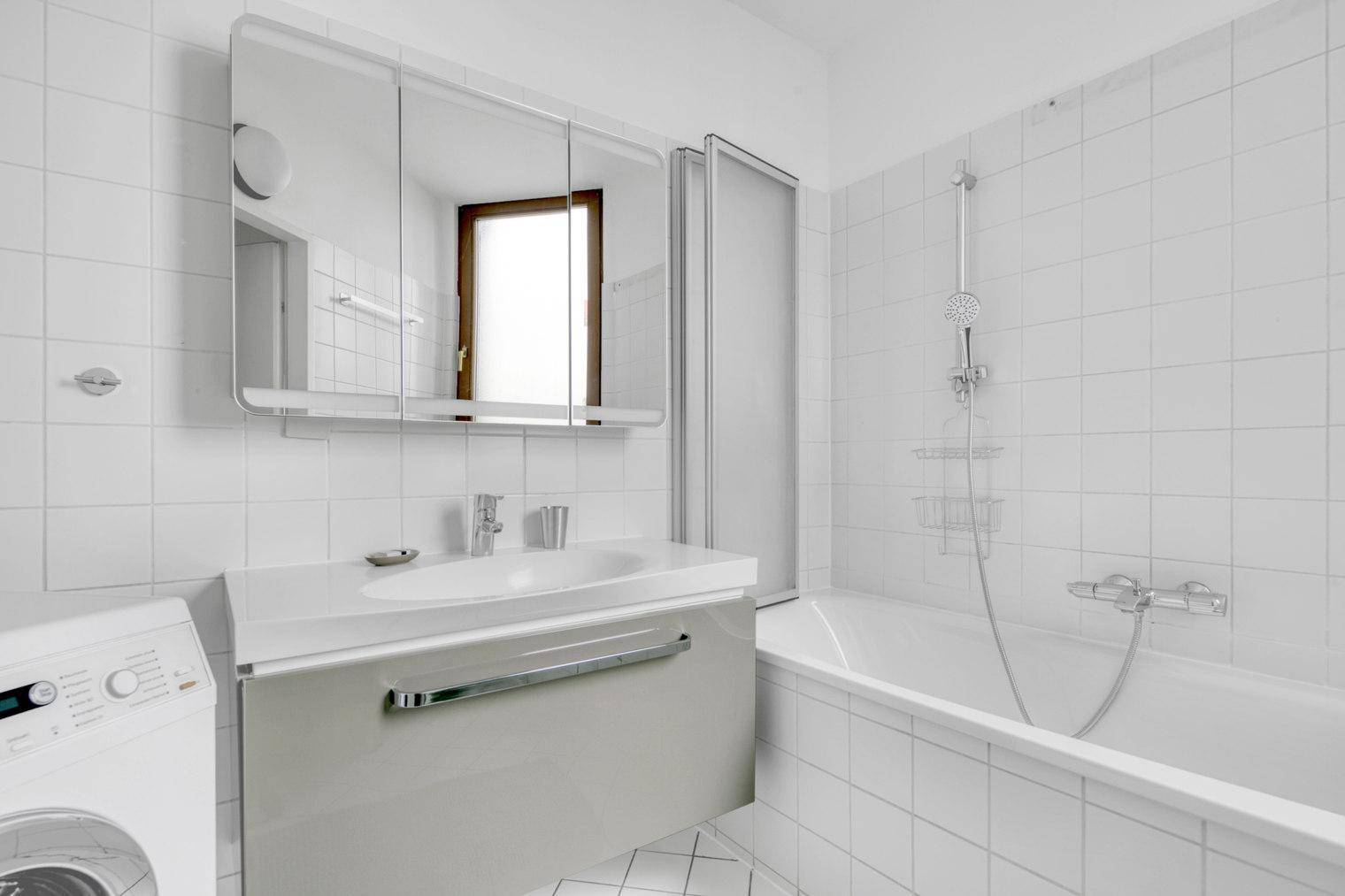 Helles Badezimmer mit Badewanne, Waschbecken, Spiegelschrank und Waschmaschine.