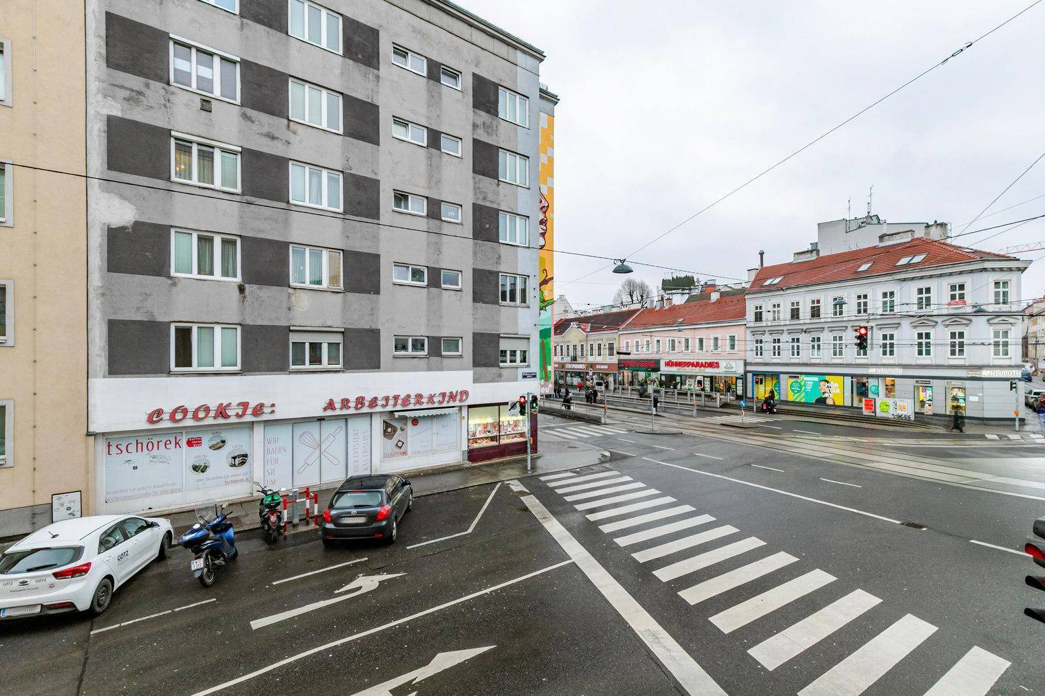 Blick aus dem Fenster auf eine belebte Stadtkreuzung mit Gebäuden und Fahrzeugen.
