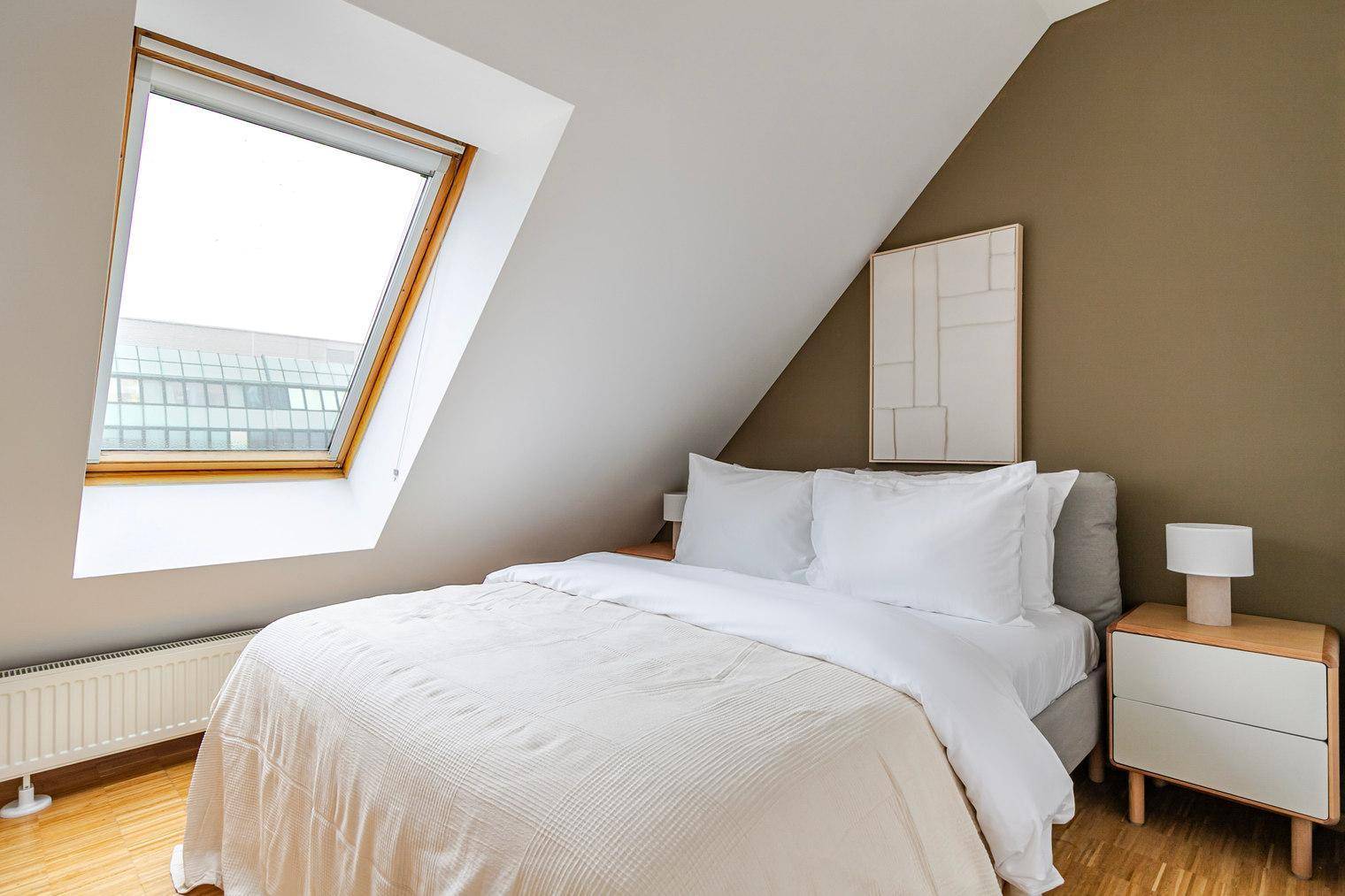 Gemütliches Schlafzimmer im Dachgeschoss mit Dachfenster, Holzboden und schräger Decke.