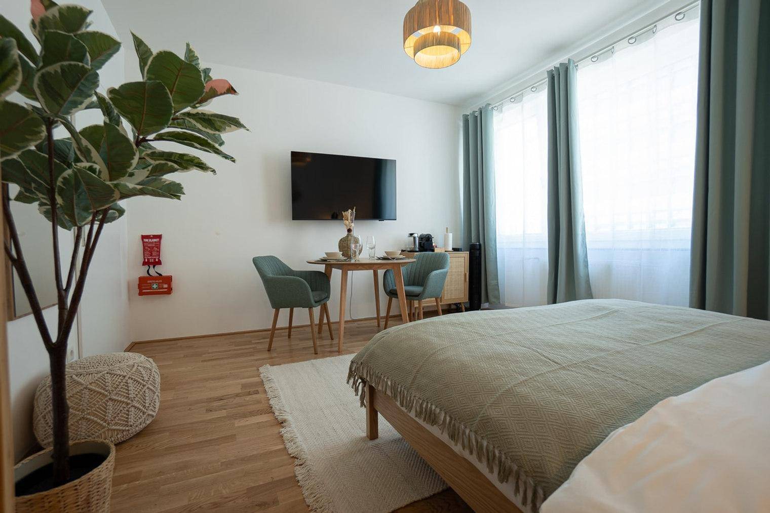 Schlafzimmer mit Doppelbett, Esstisch und großem Fenster mit Vorhängen für viel Tageslicht.